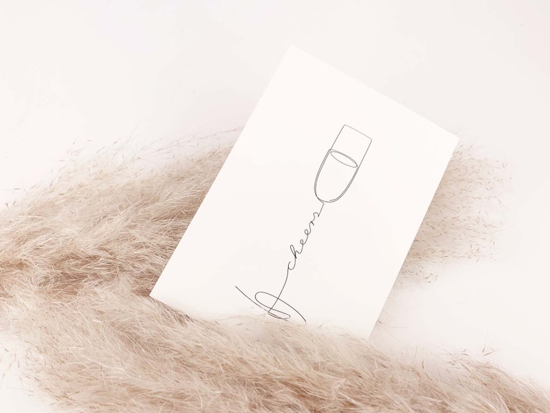 May include: A white card with a black line drawing of a champagne flute and the word "cheers" written in cursive.