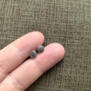 May include: A pair of small, silver stud earrings with a black, grid-like pattern.