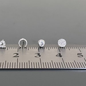 May include: Five different silver nose rings with clear rhinestones, measured on a ruler in inches.