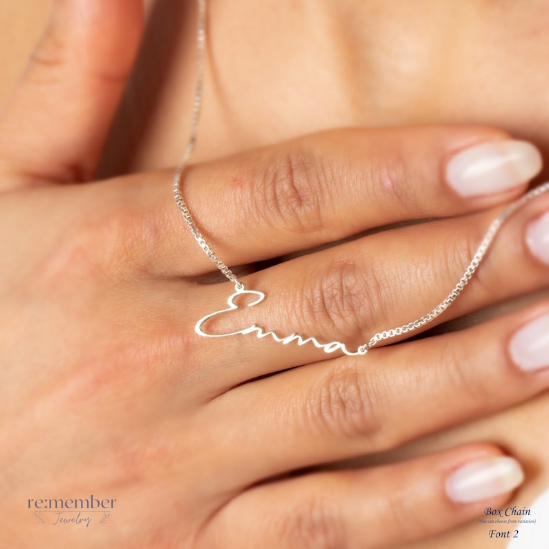 Custom silver name necklace with Emma in cursive script, shown on a womans hand. Personalized jewelry ideal for gifts, crafted with a delicate box chain. Perfect for birthdays, anniversaries, and special occasions.