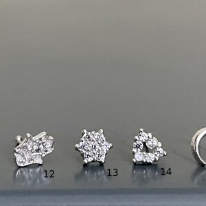 May include: A set of six silver nose rings with different designs, including an owl, a flower, a star, a heart, and a hoop. The rings are all set with clear cubic zirconia stones.