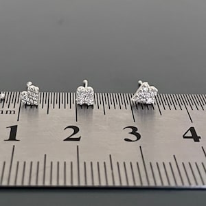 May include: Four silver nose studs with small diamond-like accents are lined up on a ruler, measuring 0.5 mm to 6 mm.