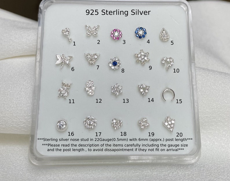 May include: A display of 20 sterling silver nose studs with various designs, including butterflies, stars, hearts, and a crescent moon. The studs are arranged in a grid on a white background. The text "925 Sterling Silver" is at the top of the display. The text "Sterling silver nose stud in 22Gauge(0.5mm) with 6mm (apprx.) post length" is at the bottom of the display.
