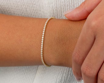 May include: A gold tennis bracelet with small round diamonds set in a pave setting.