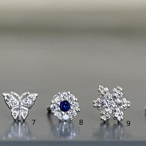 May include: A set of ten silver nose rings with different designs, including a butterfly, a flower, and a snowflake. Each ring is adorned with sparkling cubic zirconia stones.