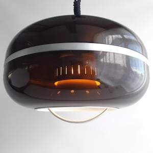 May include: A spherical pendant light fixture featuring a dark brown translucent glass shade with a horizontal silver band. Inside, a central cylindrical component emits a warm orange glow, and a silver ring hangs from the bottom opening.
