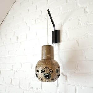 May include: A brown ceramic wall sconce with a black metal arm and a white cord. The sconce has a round, globe-shaped shade with a pattern of stars and circles.