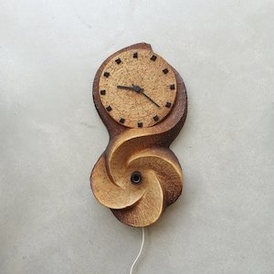 May include: A brown and tan ceramic wall clock with a swirling design and a round clock face with black hands and black numbers.