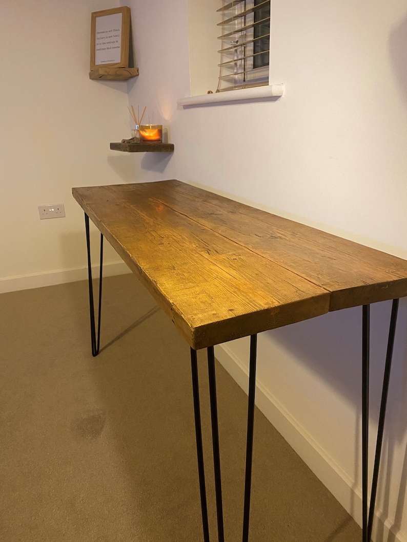 May include: A rustic wooden desk with a natural wood finish and black hairpin legs. The desk is sitting on a beige carpet.