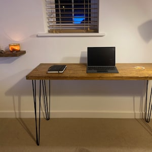 May include: A wooden desk with black hairpin legs. A laptop computer is on the desk, along with a notebook and a coaster.