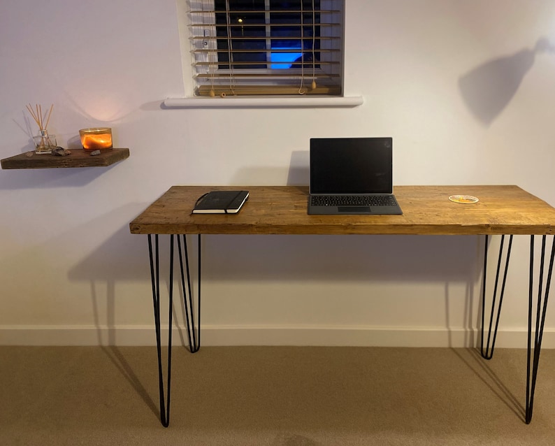 May include: A wooden desk with black hairpin legs. A laptop computer is on the desk, along with a notebook and a coaster.