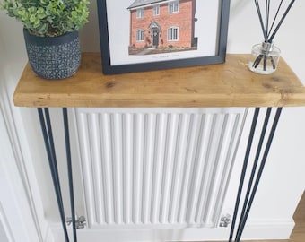 May include: A rustic wooden console table with black hairpin legs. The table is decorated with a framed house illustration, a potted plant, and a diffuser.