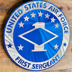 May include: A blue and silver metal sign with the words "United States Air Force First Sergeant" and five stars. The sign features a blue diamond shape with a silver roof and a silver number one.