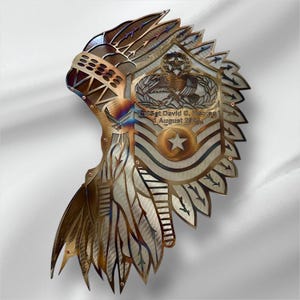 May include: A metal wall art piece depicting a Native American headdress with a US Air Force emblem and the text "E-MSgt David C. Hermosillo August 2024". The headdress is made of metal and has a brown and gold finish.