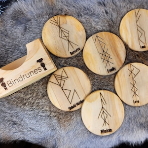 May include: Set of six wooden coasters with different Norse symbols and words, including "Luck", "Family", "Love", "Wisdom", "Shield Maiden", and "Norse", in a wooden holder labeled "Bindrunes".