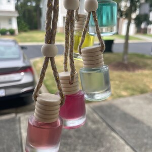 May include: Five glass bottles with colorful liquids hanging from strings with wooden beads. The bottles are clear and have a wooden cap. The bottles are hanging from a window.