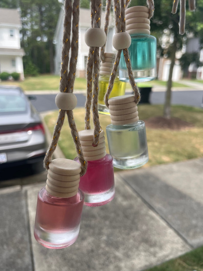 May include: Five glass bottles with colorful liquids hanging from strings with wooden beads. The bottles are clear and have a wooden cap. The bottles are hanging from a window.
