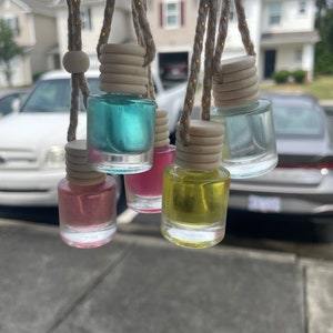 May include: Six small glass bottles with different colored liquids hanging from strings with wooden beads and caps. The bottles are hanging from a car window.