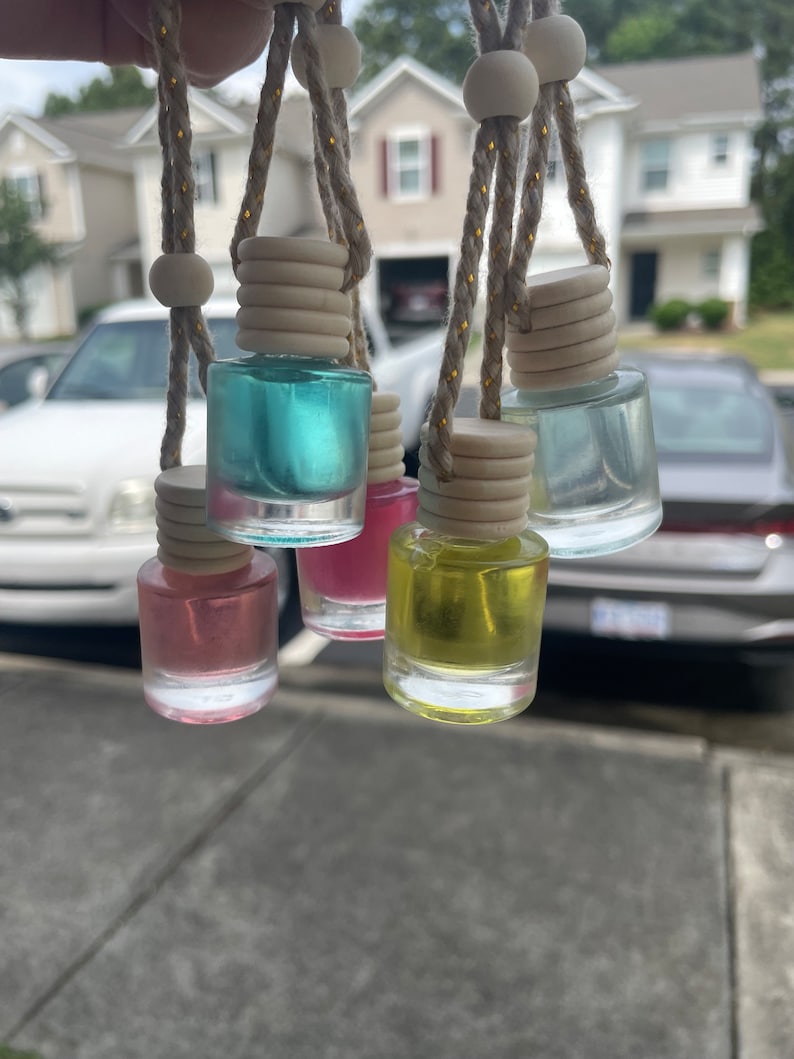 May include: Six small glass bottles with different colored liquids hanging from strings with wooden beads and caps. The bottles are hanging from a car window.
