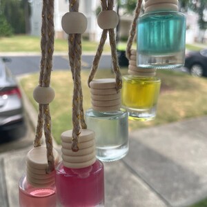 May include: Six glass bottles with different colored liquids hanging from beige cords with wooden beads. The bottles have wooden tops and are used as car air fresheners.