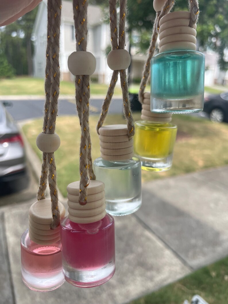 May include: Six glass bottles with different colored liquids hanging from beige cords with wooden beads. The bottles have wooden tops and are used as car air fresheners.