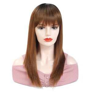 May include: A long, straight brown wig with a dark brown ombre effect and bangs. The wig is styled on a mannequin head with a pink top.
