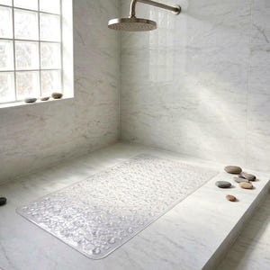 May include: A clear, rectangular shower mat with a pebble design sits on a marble floor. The shower has a rain shower head and a window with a grid pattern. Several smooth stones are placed around the shower.