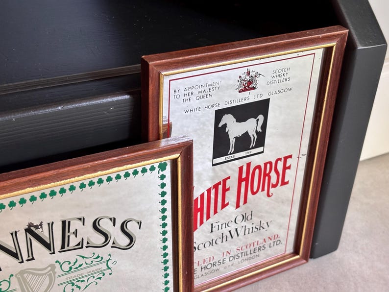 May include: Two framed vintage advertisements. One features the text "WHITE HORSE" with a white horse silhouette and "Fine Old Scotch Whisky." The other features the "GUINNESS" logo with a harp. Both have brown frames.