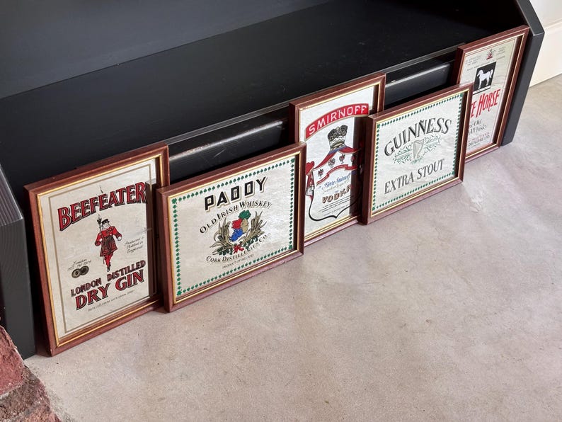 May include: A collection of framed vintage liquor advertisements, including "Beefeater London Distilled Dry Gin," "Paddy Old Irish Whiskey," "Smirnoff Vodka," "Guinness Extra Stout," and "White Horse." The frames are brown, and the ads have a vintage aesthetic.