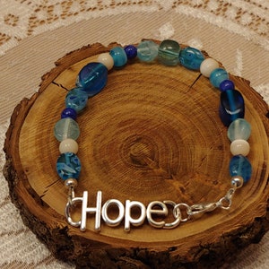 Pulsera giratoria con palabra inspiradora HOPE en tonos de azul, millefiori, ojo de gato y howlita vaquera