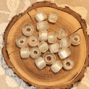 May include: A collection of clear glass beads with a silver shimmer. The beads are round and have a hole in the center. They are arranged on a wooden surface.