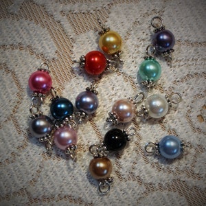 May include: Assortment of 12 pearl beads in various colors, including pink, red, blue, green, gold, black, and white. Each bead has a silver loop attached.