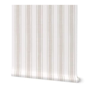 May include: A roll of wallpaper featuring a vertical stripe pattern. The design has alternating wide beige and narrow white stripes. The wallpaper is partially unrolled, revealing the pattern and texture.
