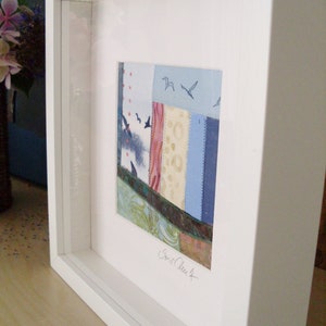 Peut inclure: Une &oelig;uvre d'art encadr&eacute;e pr&eacute;sentant un motif de patchwork color&eacute; avec des pi&egrave;ces de tissu bleu, rose et vert. L'&oelig;uvre est sign&eacute;e "Carol Clark" en bas &agrave; droite.