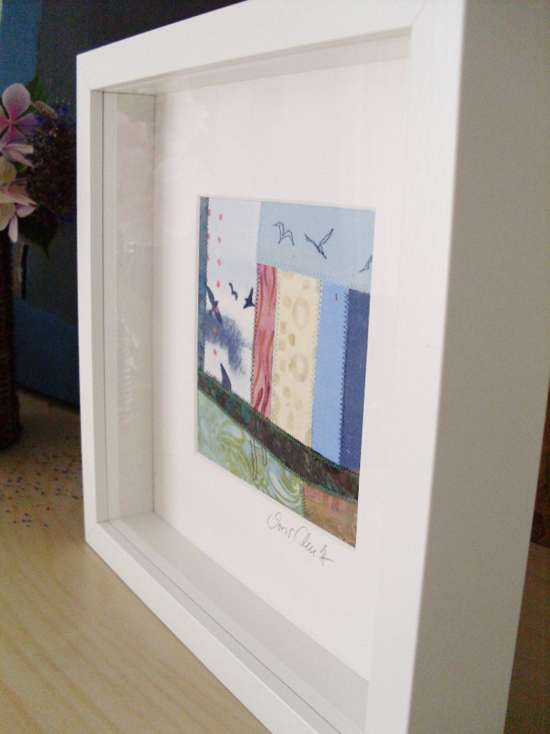 Peut inclure: Une &oelig;uvre d'art encadr&eacute;e pr&eacute;sentant un motif de patchwork color&eacute; avec des pi&egrave;ces de tissu bleu, rose et vert. L'&oelig;uvre est sign&eacute;e "Carol Clark" en bas &agrave; droite.