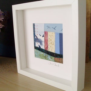 Peut inclure: Une &oelig;uvre d'art encadr&eacute;e en blanc avec un collage abstrait color&eacute; de chutes de tissu. L'&oelig;uvre d'art pr&eacute;sente une vari&eacute;t&eacute; de couleurs et de textures, notamment le bleu, le rouge, le vert et le jaune. La signature de l'artiste est visible dans le coin inf&eacute;rieur droit.