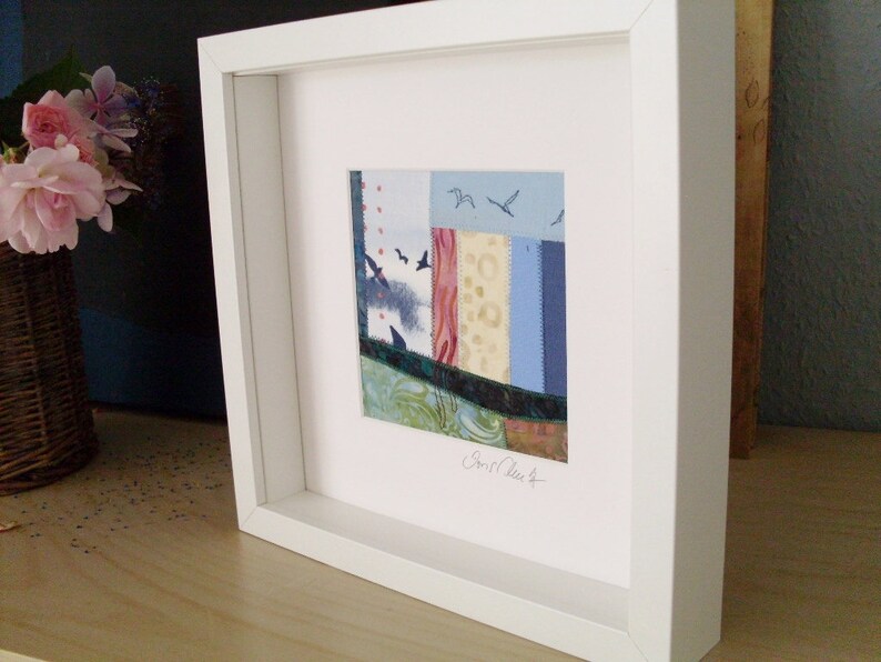 Peut inclure: Une &oelig;uvre d'art encadr&eacute;e en blanc avec un collage abstrait color&eacute; de chutes de tissu. L'&oelig;uvre d'art pr&eacute;sente une vari&eacute;t&eacute; de couleurs et de textures, notamment le bleu, le rouge, le vert et le jaune. La signature de l'artiste est visible dans le coin inf&eacute;rieur droit.