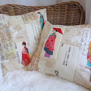 Puede incluir: Cojines decorativos con temática japonesa. Los cojines presentan un diseño de patchwork con estampados florales y de escritura. Cada cojín tiene un panel rectangular con una ilustración de geisha con un kimono colorido. Los cojines descansan sobre una superficie blanca y esponjosa.