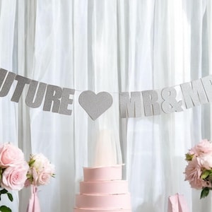 Può includere: Striscione di glitter argento con il testo "Future Mr & Mrs" e un cuore al centro. Lo striscione è appeso davanti a una tenda bianca.