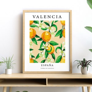 Op de afbeelding: Een ingelijst print met een aquarel-illustratie van sinaasappelbloesems en sinaasappelen op een perzikkleurige achtergrond. De tekst "VALENCIA" staat bovenaan de print en "ESPA&Ntilde;A TIERRA DE NARANJAS" staat onderaan.