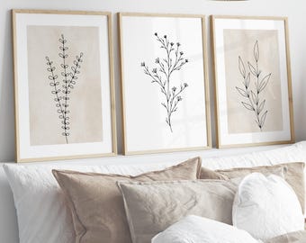 Op de afbeelding: Drie ingelijste prints met minimalistische lijntekeningen van verschillende soorten planten op een beige achtergrond. De lijsten zijn van licht hout.