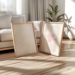 May include: Two framed art prints with light wood frames. One print features a pink bow design, the other says "I'm literally just a girl" with a pink heart. The prints are on a beige background.
