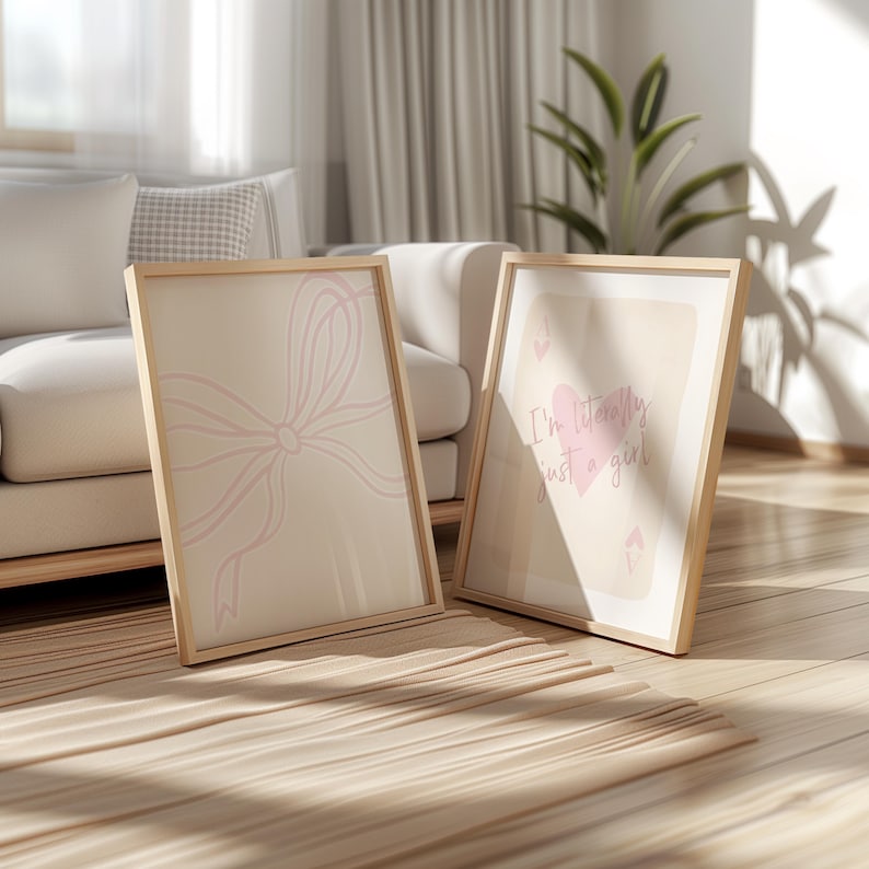 May include: Two framed art prints with light wood frames. One print features a pink bow design, the other says "I'm literally just a girl" with a pink heart. The prints are on a beige background.