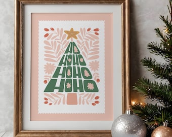 May include: A framed print featuring a pink background and a green Christmas tree design. The tree is formed from the words "Ho Ho Ho" repeated in a stylised font. The tree is surrounded by pink and green floral elements.