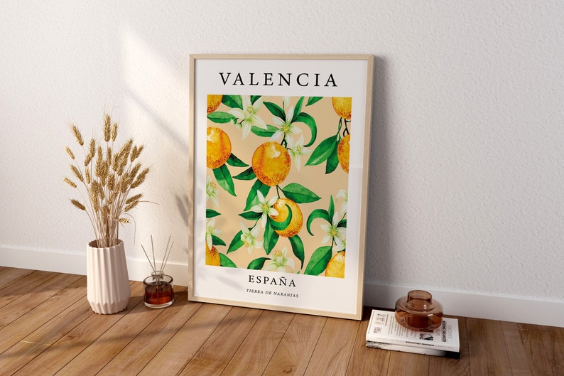Op de afbeelding: Een ingelijst afdruk met een aquarel-illustratie van sinaasappelbloesems en sinaasappelen. De afdruk heeft de tekst "VALENCIA" bovenaan en "ESPA&Ntilde;A TIERRA DE NARANJAS" onderaan.