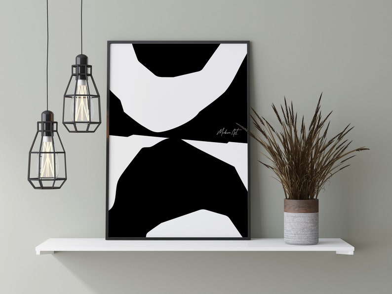 Op de afbeelding: Zwart-witte abstracte kunstprint met de tekst "Modern Art" in wit schrift. De print is ingelijst in een zwart frame en wordt getoond op een wit rek met een bruine en grijze vaas met gedroogd gras.