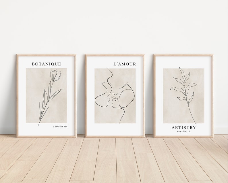 K&ouml;nnte beinhalten: Drei minimalistische Line-Art-Drucke in Holzrahmen. Der erste Druck zeigt eine einzelne Blume mit dem Text "BOTANIQUE abstract art". Der zweite Druck zeigt die Gesichter eines Paares mit dem Text "L'AMOUR". Der dritte Druck zeigt ein einzelnes Blatt mit dem Text "ARTISTRY simplicit&eacute;".