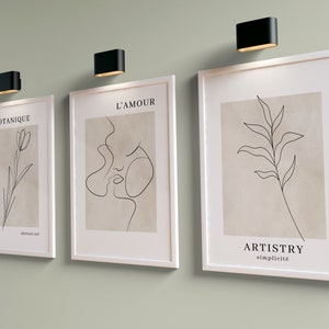 K&ouml;nnte beinhalten: Drei gerahmte minimalistische Linienkunst-Drucke mit wei&szlig;en Rahmen und beigefarbenem Hintergrund. Die Drucke zeigen eine einzeilige Zeichnung einer Blume, eines Gesichts und eines Blattes. Die Drucke sind mit "Botanique", "L'Amour" und "Artistry Simplicit&eacute;" betitelt.