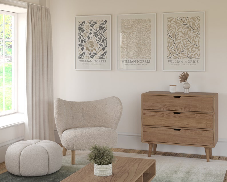 May include: Three framed prints with botanical illustrations and the text "William Morris" hanging on a white wall above a wooden dresser with three drawers. A white armchair and a white ottoman are in the foreground.