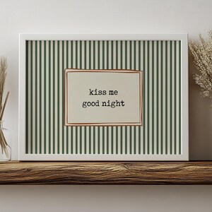 Puede incluir: Un estampado enmarcado con borde blanco. El fondo presenta rayas verticales verdes y blanquecinas. Un rect&aacute;ngulo en el centro contiene las palabras "kiss me good night" en una fuente sencilla, enmarcado por un borde marr&oacute;n.